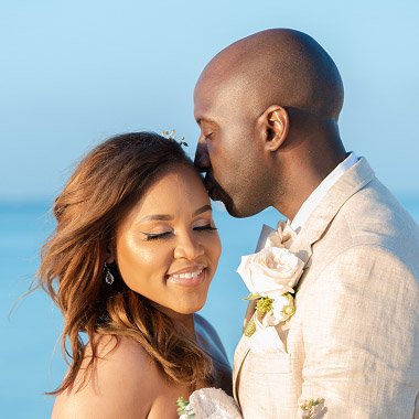 Groom kissing the bride on the forehead by the ocean